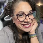 Headshot of a woman wearing glasses, red lipstick and a gray tshirt. She is smiling and looking at the camera.