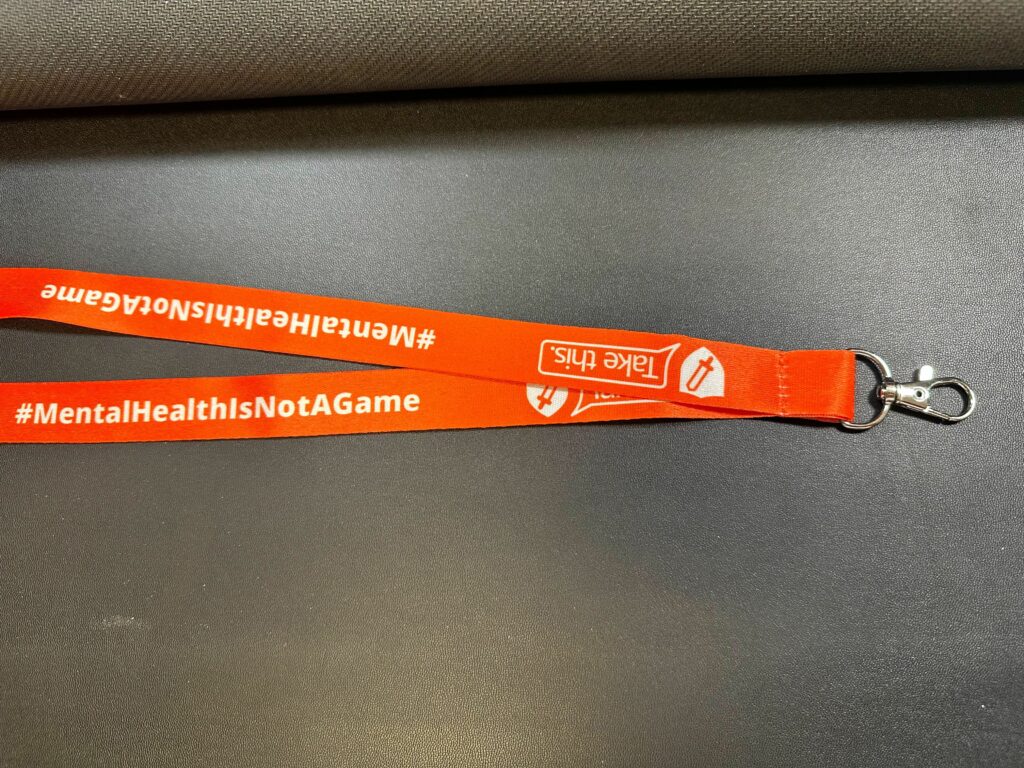 orange lanyard with the take this logo and hashtag mental health is not a game.