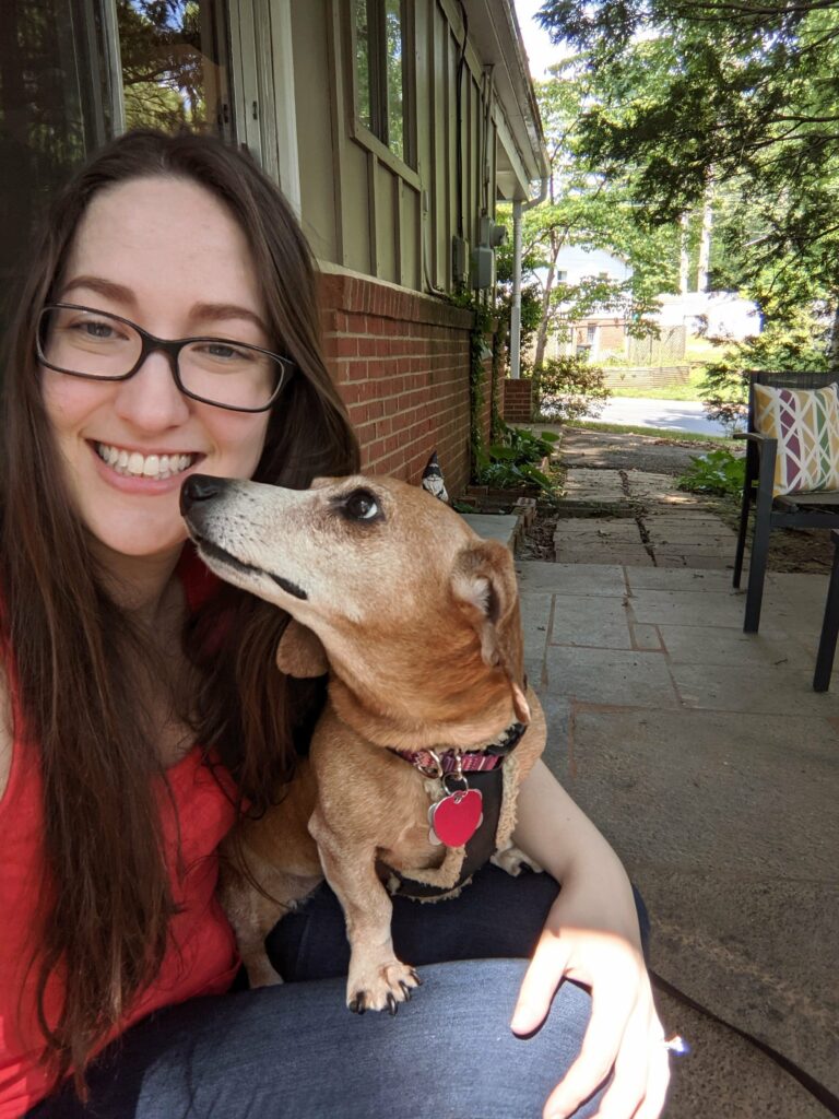 woman smiling with a small dog nuzzling her face