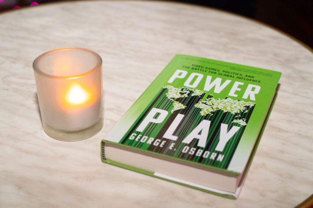 The book "Power Play" by George E. Osborn sits on a table next to a lit candle.